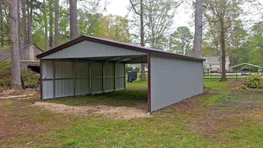 Metal carport with two walls and two gables, double wide with grey coloring and burgundy trim.