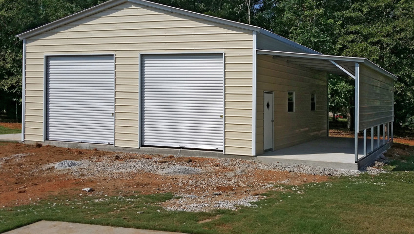 Two roll up garage doors on the front of a double wide metal garage with a lean to installed on the side of a concrete foundation.