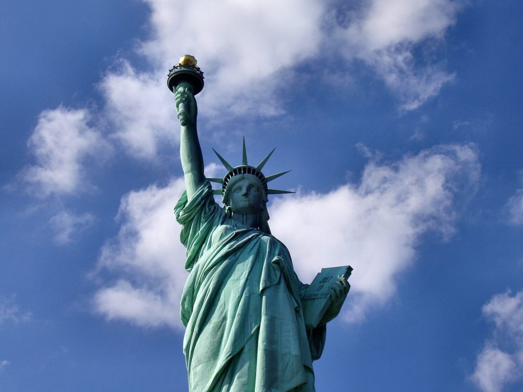 Statue of liberty stands over liberty island and underneath a blue sky